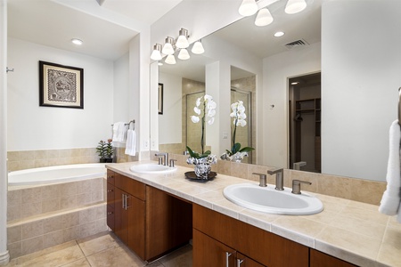 - Elegant bathroom with dual sink vanity and warm wood cabinetry   - Large mirror reflects bright lighting for a fresh and open feel   - Walk in shower and soaking tub offer versatile relaxation options
