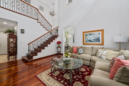 - Stylish living area featuring a curved staircase with wrought iron railing - Plush sectional seating and glass coffee table on an ornate rug - High ceilings and natural light enhance the airy, welcoming atmosphere