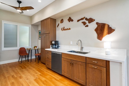 - Modern kitchen section with wood cabinetry sleek white counters and stainless steel sink - Decorative wall art and coffee station create a welcoming spot for morning routines - Warm flooring and soft lighting enhance the inviting coastal inspired design