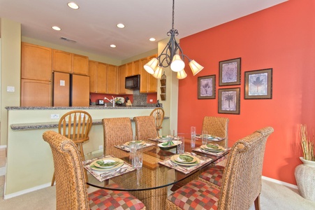 - Dining area with glass top table, wicker chairs, and place settings for six - Warm red accent wall and pendant lighting create a cozy atmosphere - Open layout connects seamlessly to the kitchen for easy serving
