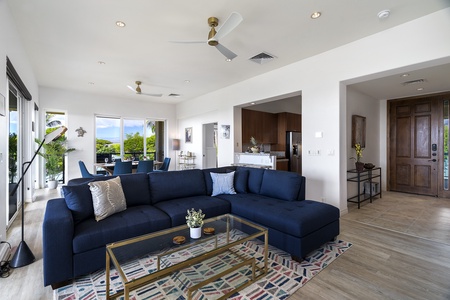 - Comfortable navy sectional anchors this bright and airy open concept   - Glass coffee table and coastal rug add style and a relaxed island vibe   - Dining area and kitchen nearby create an easy space for gatherings