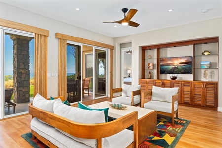 - Stylish seating area with wood framed furniture & plush cushions creating a warm welcome - Sliding doors reveal an inviting patio with views of greenery & ocean horizon - Built in shelving and wall art enhance the room’s charm and coastal inspired feel