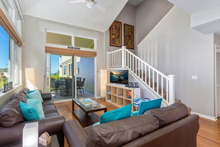- Bright and inviting living area with vaulted ceilings and modern coastal decor - Flat screen TV, plush seating, and direct access to the patio create a relaxed vibe - Stylish staircase adds charm and leads to the upstairs bedrooms