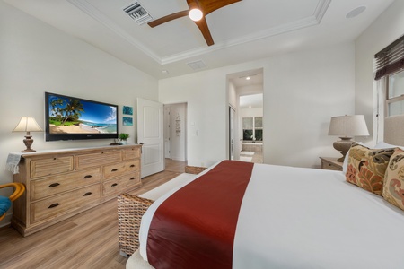 Unwind in your serene bedroom with plush bedding, warm wood furnishings, and tropical ambiance beneath elegant tray ceilings.