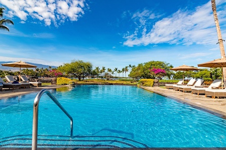 A pristine swimming pool surrounded by lush tropical landscaping, swaying palms, and vibrant gardens under blue skies—perfect for leisurely days in paradise.