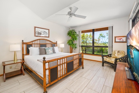 - Spacious primary bedroom with a tropical wood king bed and neutral tones throughout - Large window brings in beautiful garden views and natural sunlight - Ceiling fan, comfy reading chair, and tile floors create a cool, restful space to unwind