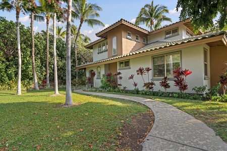 Mediterranean-style villa nestled among swaying palms and tropical gardens, featuring tile roofing and warm stucco exterior in a peaceful residential setting.