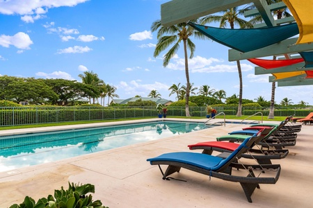 Colorful lounge chairs under shade sails beside a pristine pool.