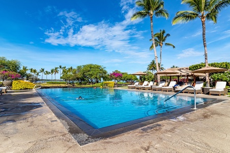 A sparkling pool surrounded by palm trees and tropical gardens, with lounge chairs and a thatched-roof cabana ready for your island escape.