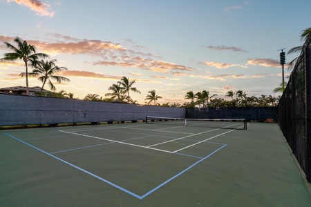 Tennis court surrounded by swaying palms under tropical sunset skies, offering recreational activities in a resort setting.
