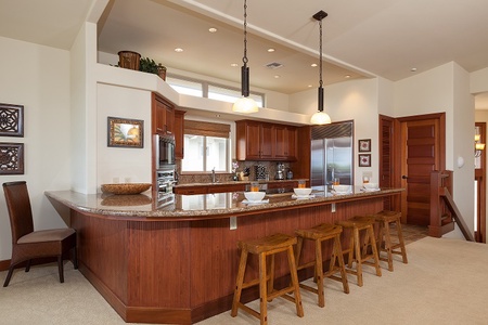 - Spacious kitchen with curved granite island and four bar stools   - Rich wood cabinetry and stainless steel fridge offer style and function   - Warm lighting and open layout make this a welcoming gathering spot