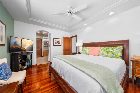 - Elegant bedroom with king bed, tray ceiling, and hardwood flooring - Arched doorway provides direct access to the ensuite bathroom - Warm wood finishes and tropical touches create a serene retreat