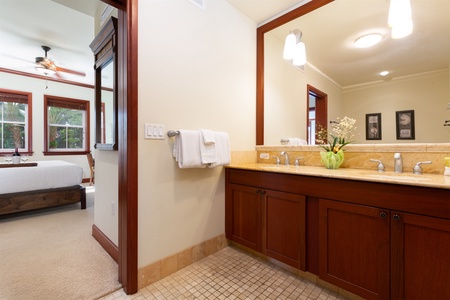 - Bathroom with warm wood vanity, large framed mirror, and soft lighting   - Neutral tile flooring adds texture and a clean, classic style   - Convenient layout connects directly to the adjoining bedroom for privacy