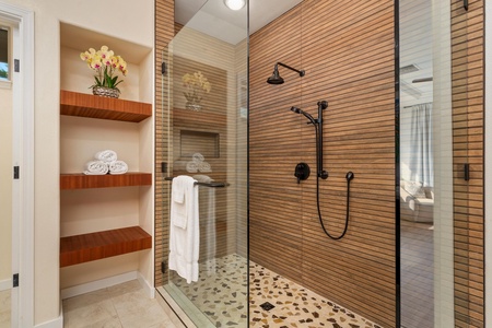 Step into your spa-like glass shower featuring warm wood walls, rainfall head, and handheld sprayer for the ultimate relaxation.
