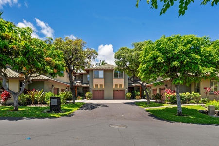 Gated driveway entry lined with greenery leads to a charming two story villa.