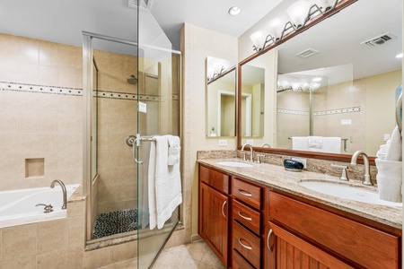 En suite primary bathroom with dual sinks, granite countertops, bathtub and walk in shower