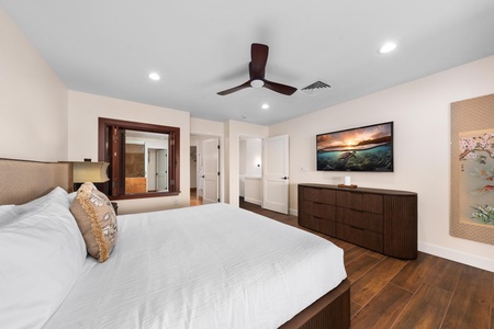 Your peaceful master bedroom features a plush king bed, rich wood floors, and a stunning ocean sunset view on the mounted TV.