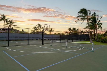 Multi-sport court with tennis net and basketball hoop surrounded by tropical palms under golden sunset skies.