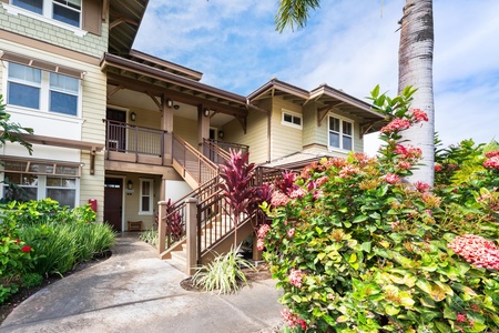 Tropical property exterior featuring lush landscaping with vibrant flowering plants and palm trees surrounding the building entrance.
