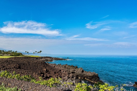 Stunning volcanic coastline with dramatic black lava rocks meeting crystal blue Pacific waters under tropical skies.