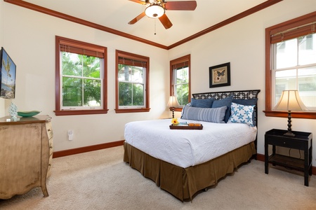 - Cozy bedroom with queen bed, crisp white bedding, and decorative pillows   - Three large windows bring in natural light and garden views   - Ceiling fan and warm wood trim add charm and comfort to the space