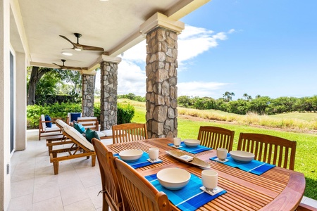 - Stylish covered terrace with stone pillars framing views of greenery and open skies - Long wooden dining table set with dishware and vibrant blue accents for gatherings - Ceiling fans and open design create a breezy inviting atmosphere for any occasion