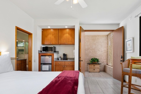 - View from bed reveals a functional kitchenette and tranquil outdoor stone patio - Coffee bar essentials and a mini fridge ensure comfort and independence - Patio seating just steps away offers fresh air and peaceful morning starts