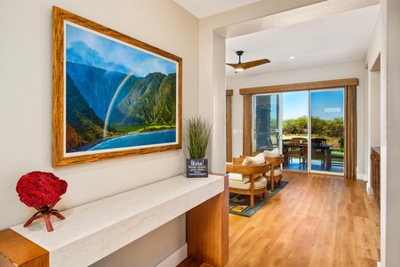 - Console table with stone top and wood frame positioned beneath vibrant landscape artwork - Hallway opens to living area with large sliding doors and outdoor scenery - Decorative accents and natural light enhance the inviting feel of the home’s interior