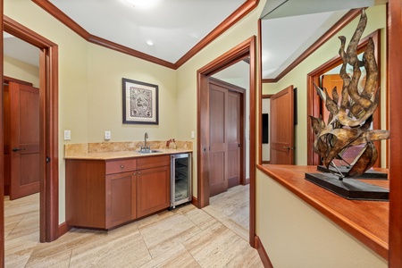 Step into your private retreat featuring elegant wood accents and warm stone floors. A wet bar with mini-fridge awaits your convenience, while rich cabinetry and artwork create a welcoming ambiance.