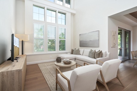 Relax in your bright, airy living space where natural light streams through tall windows onto plush seating and warm wood floors.