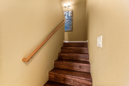 Rich wood stairs lead you upward, guided by a smooth handrail and warm lighting. Elegant artwork adds character to your journey between levels.
