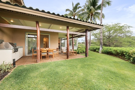 Modern tropical home featuring covered lanai with BBQ station, lush landscaping with palm trees, and manicured lawn.