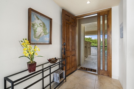 - Welcoming entryway with warm wood door and tropical floral arrangement   - Tile flooring and wall art create a bright cheerful first impression   - Leads directly to the open living and dining spaces beyond