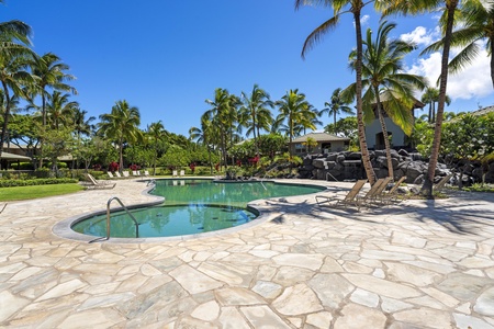 Tropical pool area with swaying palms, stone deck, and hot tub surrounded by lush landscaping and volcanic rock features.