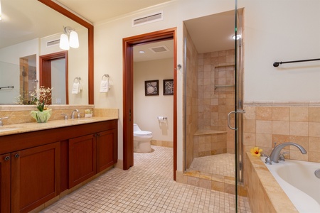 - Spacious bathroom with wooden vanity and beige stone tile accents   - Walk in shower with glass door and built in bench for added comfort   - Warm lighting creates a spa like atmosphere