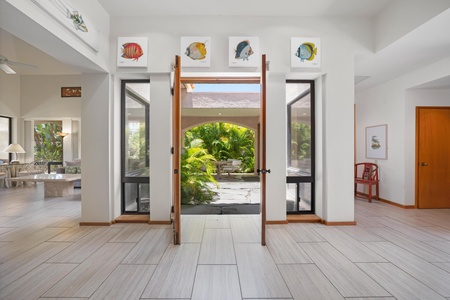 - Double glass doors open to a beautiful tropical garden for a seamless indoor outdoor vibe - Framed fish artwork adds a playful coastal touch above the entryway - Natural light pours in through floor to ceiling windows on both sides
