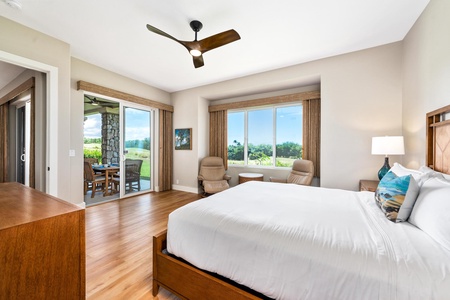 - Spacious bedroom with large window framing scenic greenery and ocean horizon - Sliding glass door opens to a covered patio with seating for fresh air relaxation - Two recliners and side table create a cozy reading or lounging corner