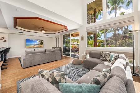 Relax in your spacious living room with plush sectional seating and tropical garden views through floor-to-ceiling windows.