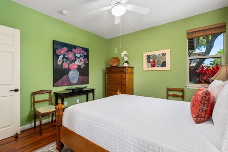 - Green walled bedroom with wooden furniture and vibrant floral artwork - Chest of drawers, chairs, and decor add a classic touch to the room - Ceiling fan provides comfort for a restful night’s sleep