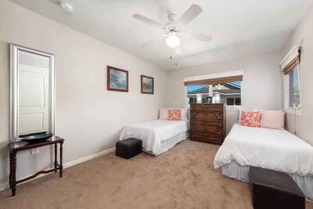 - Two twin beds flank a wooden dresser beneath bright windows with natural light - Decorative pillows and ocean inspired artwork add a coastal touch - Ceiling fan and carpeted floors make this space fresh and inviting