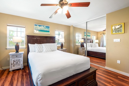 Sink into crisp white linens and rich wood furnishings in your bedroom retreat. Natural light streams through multiple windows, while ceiling fan and warm tones create a cozy, comfortable atmosphere.