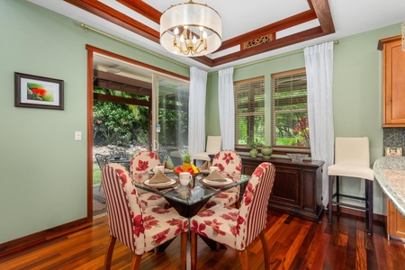 - Bright dining room with floral chairs, glass top table, and chandelier - Surrounded by large windows with views of the garden and patio - Warm wood floors and soft green walls create a welcoming atmosphere
