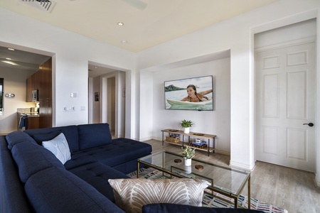 - Cozy media space with navy sectional facing a large wall mounted TV   - Neutral walls and coastal accents create a relaxing entertainment area   - Ideal for movie nights or watching your favorite shows in comfort