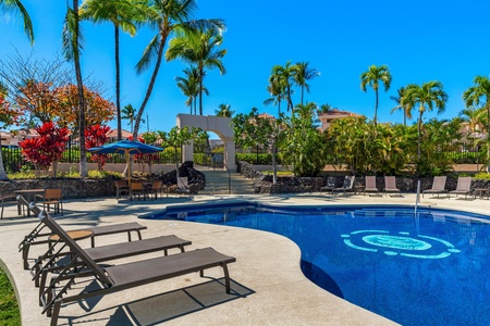 Sparkling pool surrounded by swaying palms and tropical blooms, where sun-soaked loungers await your arrival beneath brilliant blue skies.