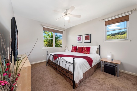 - Rest easy in this cozy guest room featuring a plush bed with bold red decor - Surrounded by tropical greenery, views peek through two bright windows - Ceiling fan and soft carpeting create a peaceful and breezy atmosphere