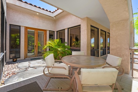 - Shaded patio with a round dining table and padded chairs for relaxed outdoor meals - Surrounded by sliding glass doors and tropical greenery for an inviting garden vibe - Open sky cutout above lets in natural light while keeping things breezy