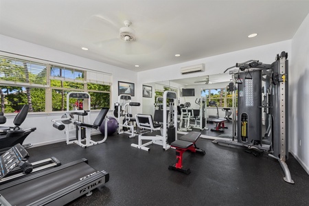 Fully equipped gym with strength training machines and tropical views through the windows.