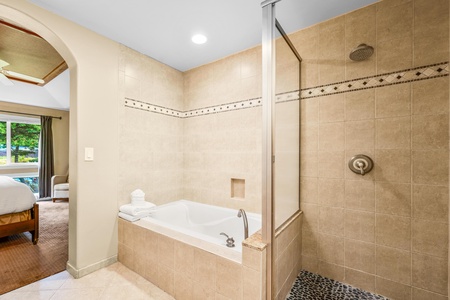 En suite primary bathroom with dual sinks, granite countertops, bathtub, and walk in shower