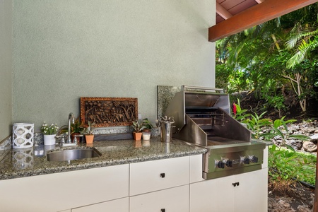 - Outdoor kitchen with granite countertop, stainless steel grill, and sink - Decorative wall art and potted plants add charm to the cooking space - Ideal setup for preparing fresh meals while enjoying the open air
