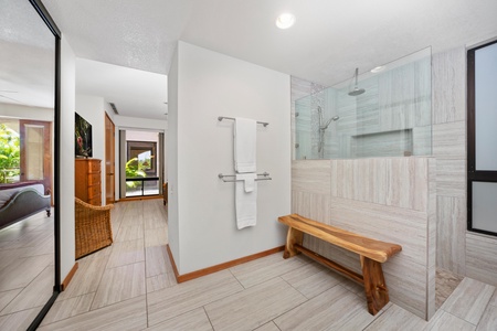 - Spacious walk in shower with modern tile and rainfall showerhead for a spa like experience - Rustic wood bench adds charm and comfort in the sleek bathroom layout - Convenient hallway access connects bedroom and bath seamlessly